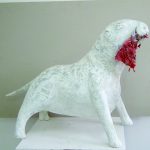 Rzeźba przedstawia białego psa z czerwoną szmatą w pysku.