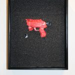 W metalowej gablocie za szkłem znajduje się pogryziony fragment zabawki - czerwonego pistoletu. Element wyeksponowany jest jak artefakt archeologiczny.